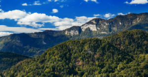 Scenatičen pogled na gorski masiv s prehajajočimi oblaki in razgibanimi vrhovi, prekrit z gostimi gozdovi.