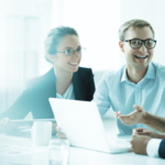 Skupina oseb sedi za mizo z odprtim prenosnikom in razpravlja o poslovnih temah.